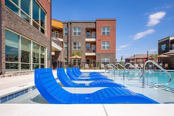 a pool with blue lounge chairs in front of an apartment building